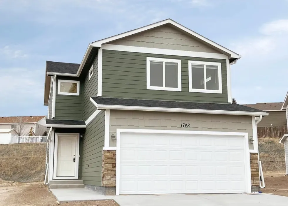 Two-story Monument home with green siding, stone accents, and a white garage door